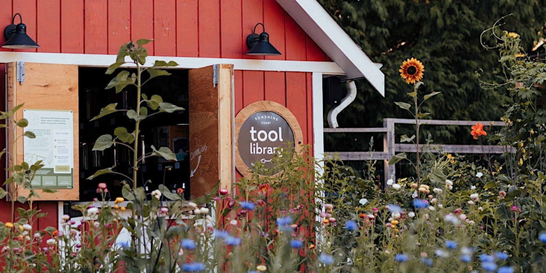 Barn with a sign saying "tool library" and lush flower beds